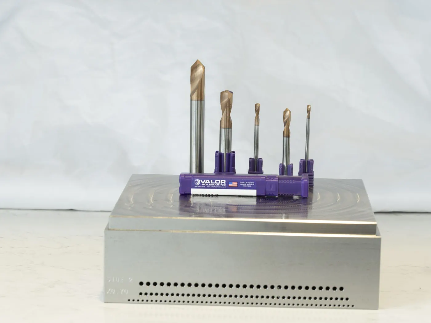 Five Valor holemaking high performance spot drills displayed on top of a workpiece with a purple product packaging container in front 