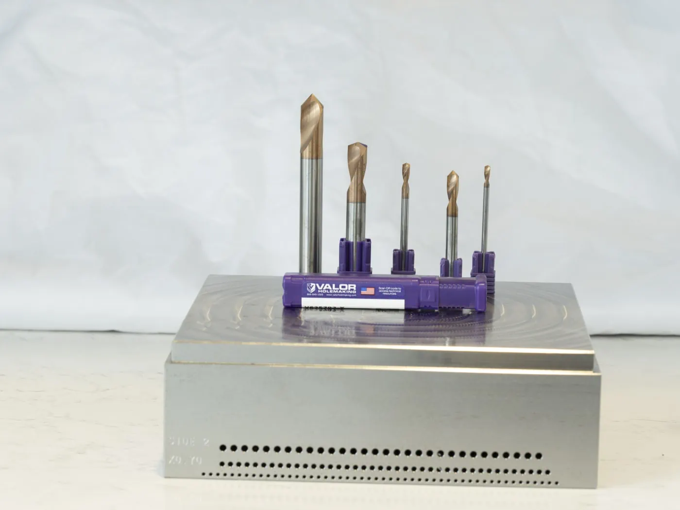 Five Valor holemaking high performance spot drills displayed on top of a workpiece with a purple product packaging container in front